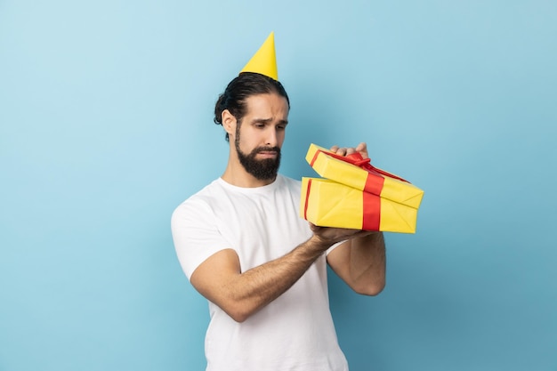 Cone de festa de homem olhando para dentro da caixa de presente e expressando tristeza esperava receber outro presente