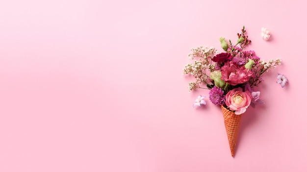 Cone de gelado com flores cor-de-rosa e folhas no fundo pastel punchy.