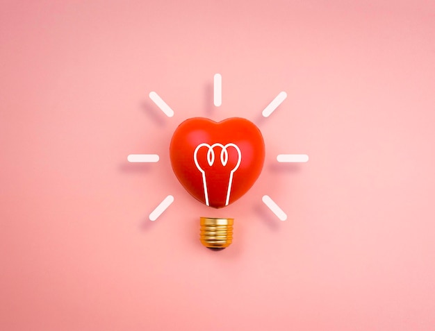 Ícone de lâmpada na bola de um coração vermelho sobre fundo rosa pastel, estilo minimalista. Amor, cuidado, compartilhamento, doação, bem-estar, inspiração e conceitos de ideias.