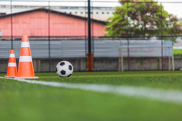 Cone de táticas de bola de futebol no campo de grama com fundo de treinamento