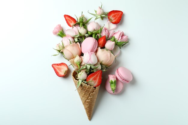 Cone de waffle com flores, morango e macaroons em fundo branco