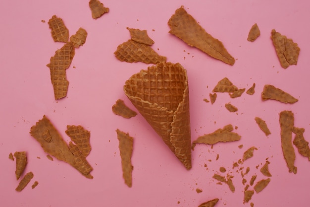 Cone de waffle destruído em fundo rosa pastel.