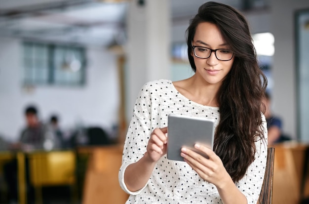 Conectado durante todo o dia de trabalho Foto de uma jovem usando um tablet digital enquanto está sentado em um escritório moderno