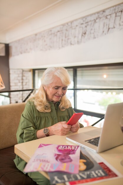 Foto conectado. elegante mujer senior sentada con un teléfono inteligente en las manos