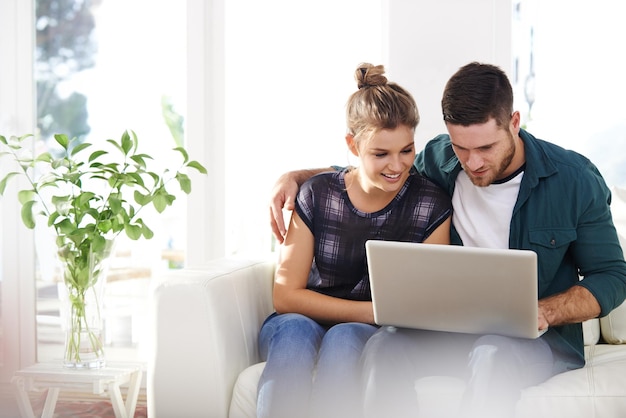 Conectado em mais de uma maneira Foto de um jovem casal feliz usando um laptop enquanto relaxa em casa juntos