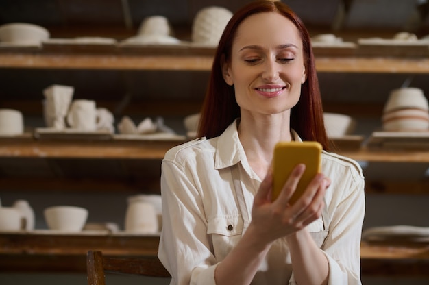 Conectado. Mulher jovem e bonita com um smartphone em uma oficina de cerâmica