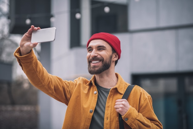 Conectados. Homem de chapéu vermelho segurando o telefone e fazendo selfie