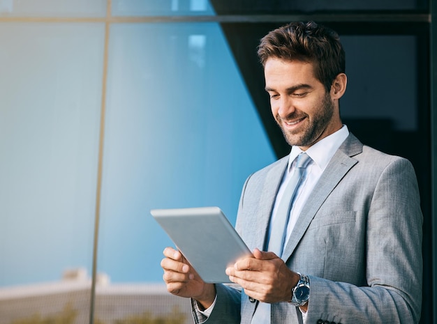 Conectando-se à cidade Foto de um jovem empresário bonito usando um tablet digital fora de um prédio de escritórios