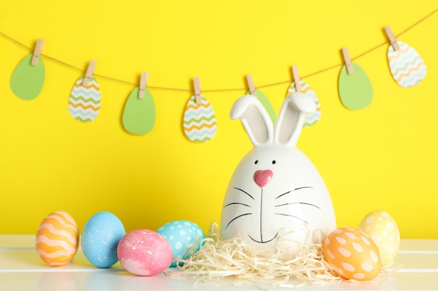 Conejito decorado y huevos de Pascua en la mesa contra el fondo de color