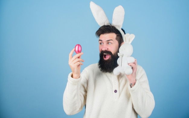 Conejito y huevo Celebración de las vacaciones de primavera Hombre barbudo con juguete de conejito y huevo de Pascua Hipster con largas orejas de conejo con liebre ponedora de huevos Conejito de Pascua entregando huevos de colores copia espacio