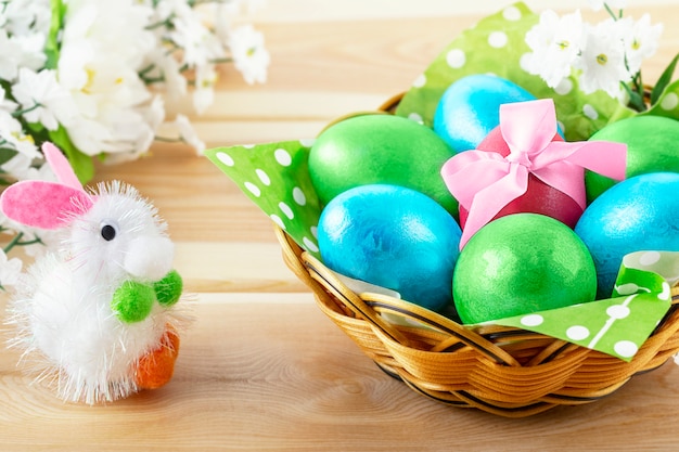 Conejito de juguete en mesa de madera y canasta con huevos decorados