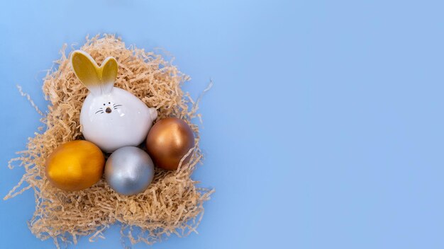 Un conejito de Pascua blanco con huevos pintados multicolores sentado en un nido casero sobre un fondo azul.