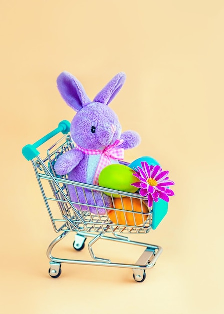 Conejito de Pascua en un carrito de compras con huevos de colores y una flor.