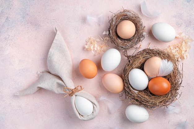 Conejito de Pascua hecho de servilletas y huevos en un nido sobre un fondo rosa claro El concepto de una feliz Pascua Vista superior