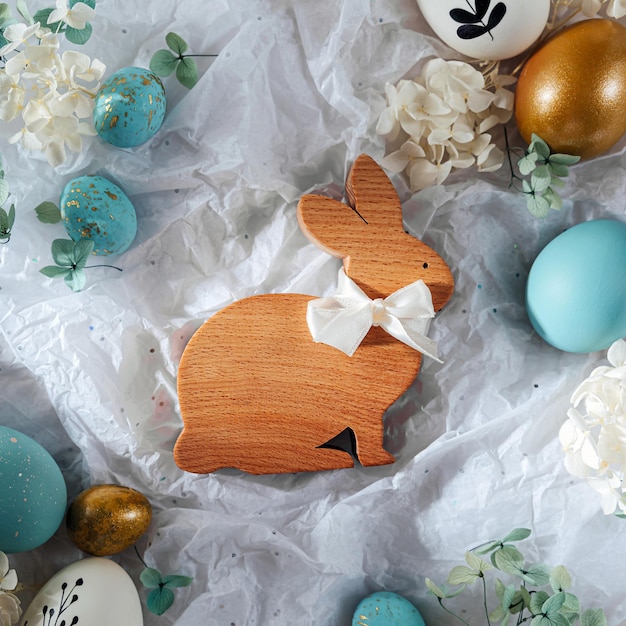 Conejito de Pascua y huevos de Pascua con dulces y flores en papel blanco Tarjeta de Pascua feliz Huevos blancos azules y dorados en papel de regalo