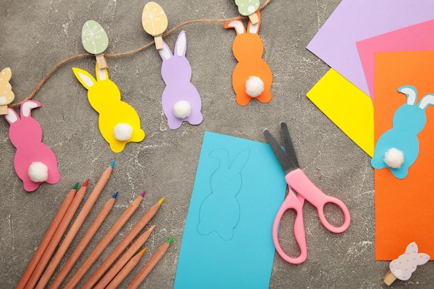 Conejitos de Pascua hechos a mano con papel de colores, manualidades fáciles para niños sobre un fondo gris.