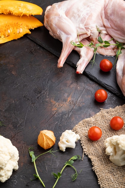 Conejo entero crudo con calabaza, tomates, brotes de guisantes sobre un hormigón negro