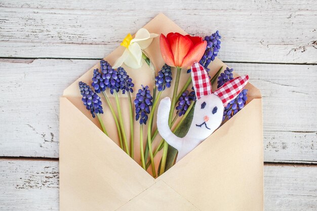 Conejo y flores en un sobre sobre fondo de madera pascua