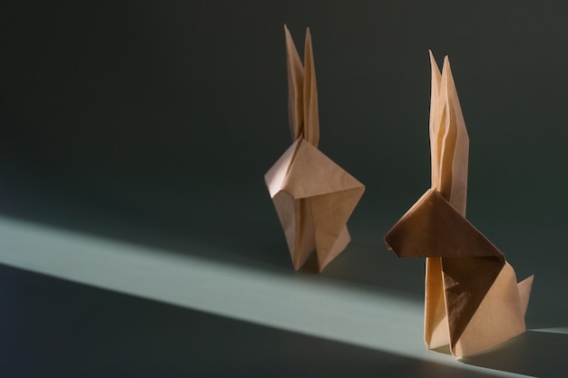 Conejo de papel de origami en el sol brillante con sombras duras. Artesanía de papel. El concepto mínimo de Pascua o el año del conejo. El juego de luces y sombras.