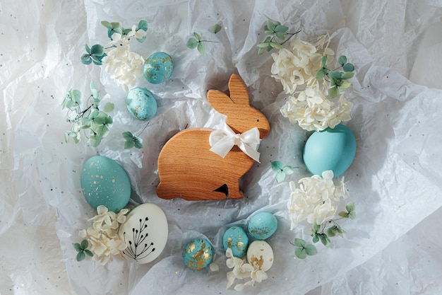 Conejo de Pascua y huevos de Pascua con dulces y flores en papel blanco Tarjeta de Pascua feliz Huevos blancos y azules en papel de regalo