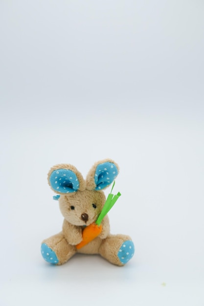 Foto conejo de pascua de juguete relleno con zanahoria contra un fondo blanco
