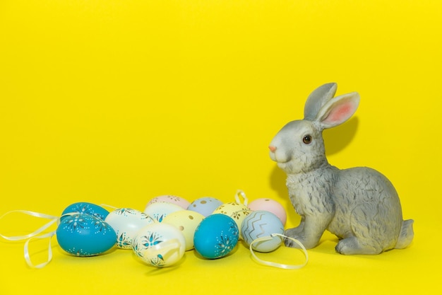 Conejo de Pascua sentado entre huevos multicolores aislado sobre fondo amarillo Concepto de vacaciones de Pascua