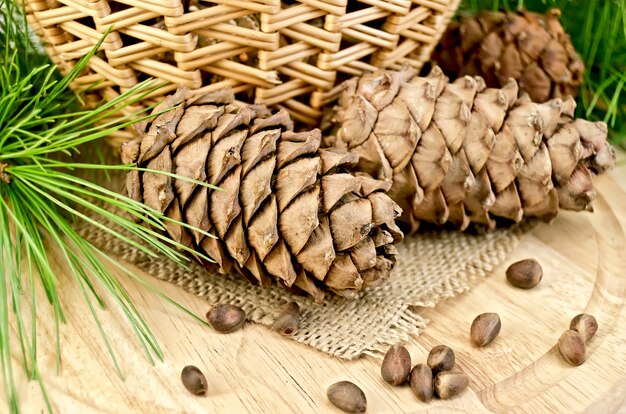 Cones de cedro, nozes, galhos verdes, cesta de vime em um fundo de pano de serapilheira e placa de madeira