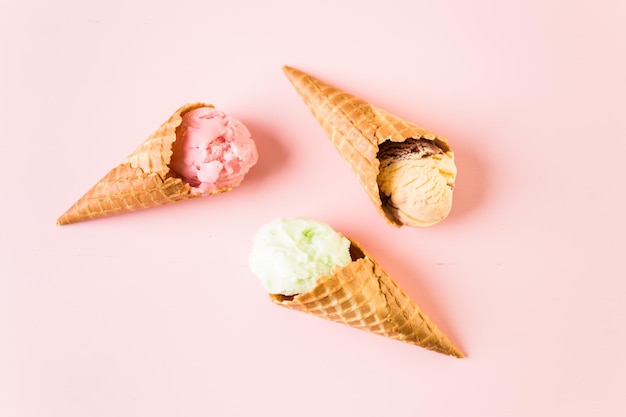 Cones de sorvete waffle com prato de colheres de sorvete em um fundo rosa.