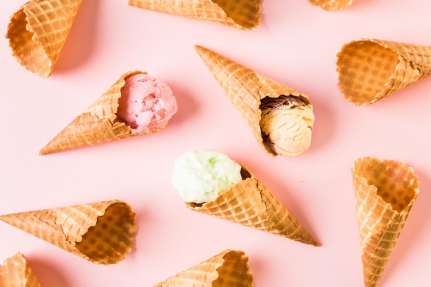 Cones de sorvete waffle com prato de colheres de sorvete em um fundo rosa.