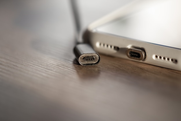 Foto conexión de un cable magnético a un teléfono inteligente para cargar, primer plano sobre un fondo de madera.