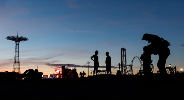 Coney Island Beach in New York City. Schattenbilder der Leute und des Fallschirmsprungturms auf einem Sonnenuntergangshintergrund