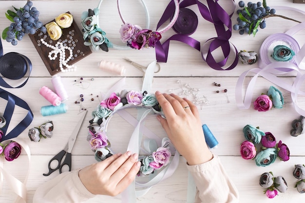 Confecção de bandanas artesanais, oficina em casa. Artista de mulher irreconhecível decorando aro de cabelo com flores e fitas, vista superior. Arte, artesanato, conceito criativo