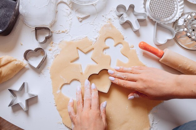 Confecção de biscoitos caseiros. Sobre a mesa está a massa e um conjunto de formas de biscoito com outros equipamentos de cozinha. Biscoitos de bebê fofo em forma de uma pessoa, um coração e uma estrela. Cozinhar com ferramentas de cozimento.