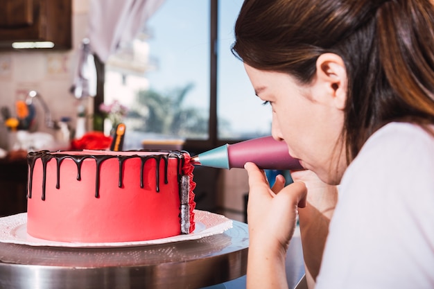 Foto confeiteira jovem decorando um bolo com chocolate