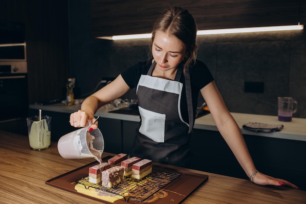 Confeiteiro feminino sorridente derramando gommage de chocolate líquido no bolo de biscoito em forma de metal trabalhando no restaurante de serviço de catering Chef de mulher de uniforme na montagem do processo de sobremesa de mousse