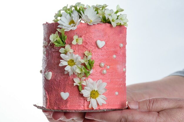 Confeiteiro segurando um bolo de chocolate coberto com creme de manteiga rosa. decorado com corações, pérolas e flores brancas.