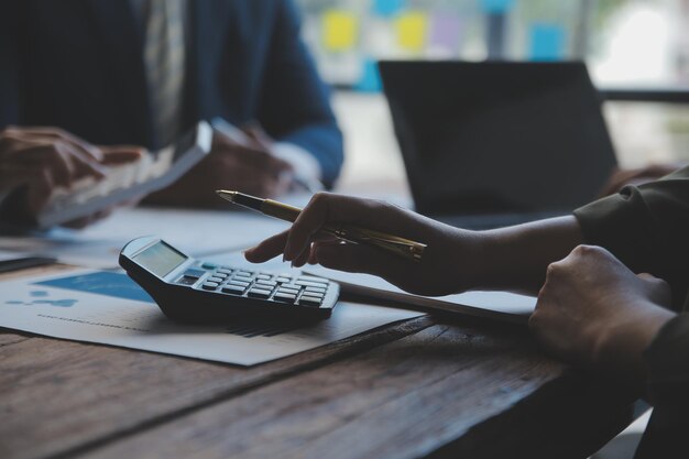 Conferência de cooperação Reunião da equipa de negócios Colegas investidores presentes a discutir novos dados de gráficos financeiros do plano na mesa do escritório com portátil e tablet digital Contabilidade financeira investimento