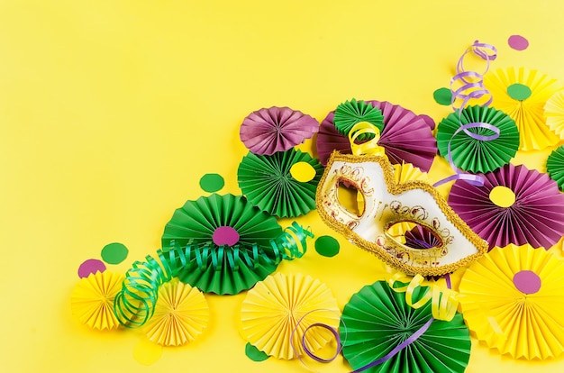 Confete de papel colorido, máscara de carnaval e serpentina colorida em um fundo amarelo