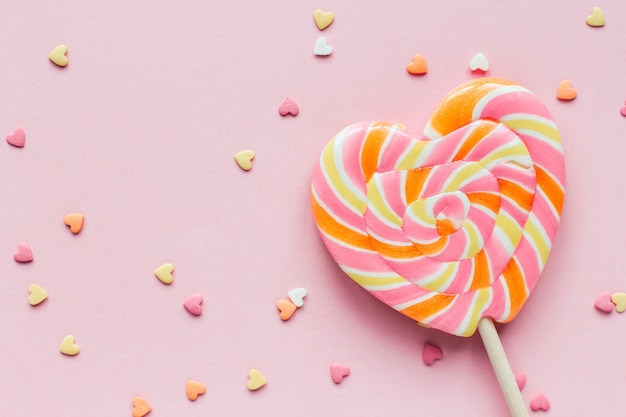 Confete pirulito e confeitaria em forma de coração listrado grande em um espaço de cópia de fundo rosa