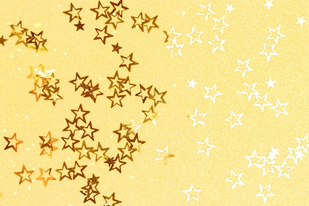 Confetes de estrelas brilhantes de cor dourada brilhante em um fundo amarelo