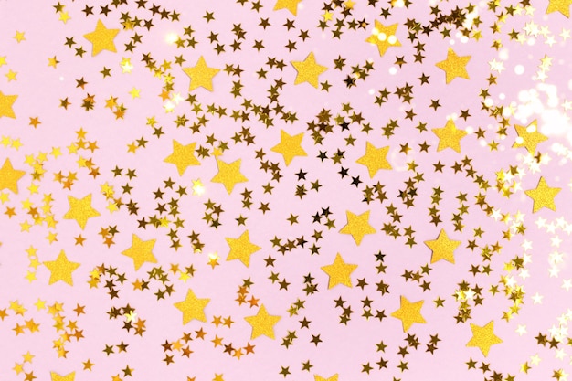 Confetes de estrelas brilhantes douradas espalhadas em um fundo roxo pastel