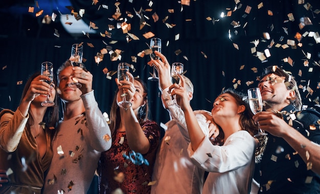 Foto el confeti está en el aire. grupo de amigos alegres celebrando el año nuevo en el interior con bebidas en las manos.