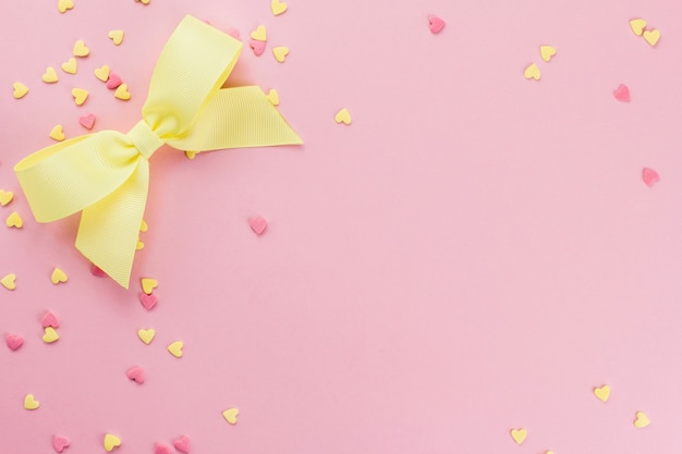 Confeti de confitería en forma de corazón amarillo y rosa y lazo amarillo sobre un espacio de copia de fondo rosa