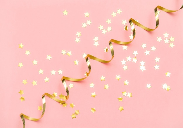 Confeti dorado y serpentina sobre fondo plano de color rosa