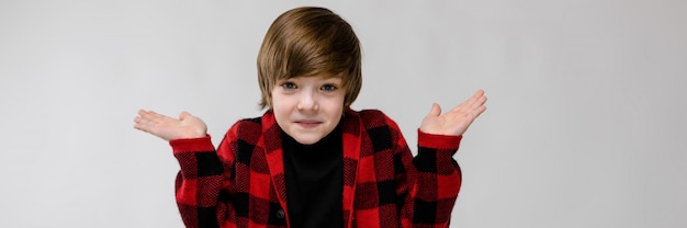 Confía en el lindo niño caucásico desconcertado en camisa a cuadros en la pared gris