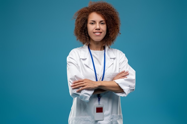 Confiada doctora en bata de laboratorio de pie con los brazos cruzados