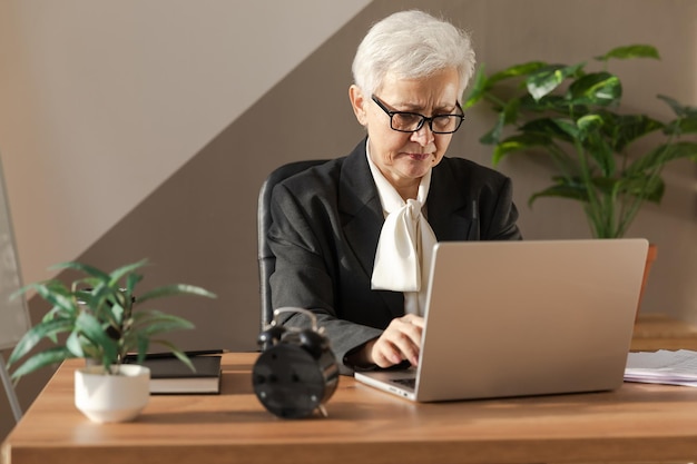 Confiada y elegante mujer mayor europea de mediana edad que usa una computadora portátil en el lugar de trabajo