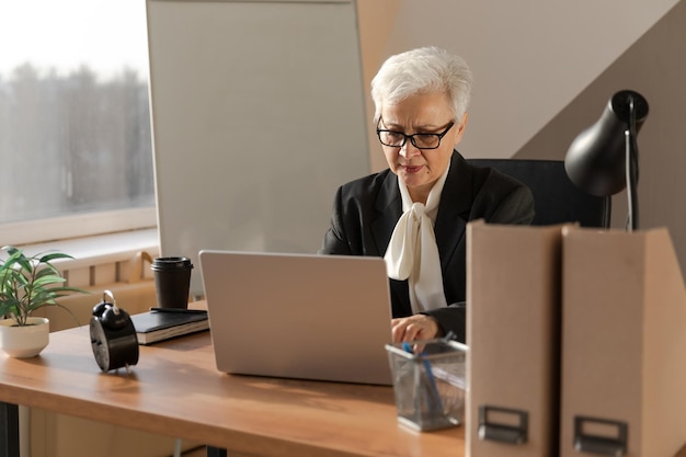 Confiada y elegante mujer mayor europea de mediana edad que usa una computadora portátil en el lugar de trabajo