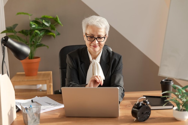 Confiada y elegante mujer mayor europea de mediana edad que usa una computadora portátil en el lugar de trabajo
