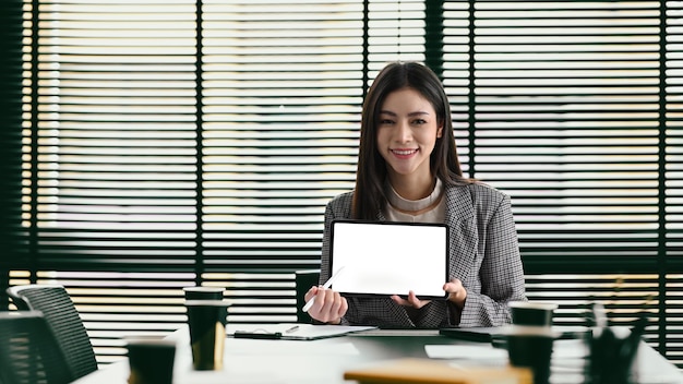 Confiada empresaria milenaria en traje formal sosteniendo tableta digital y sonriendo a la cámara Pantalla en blanco para su texto de publicidad